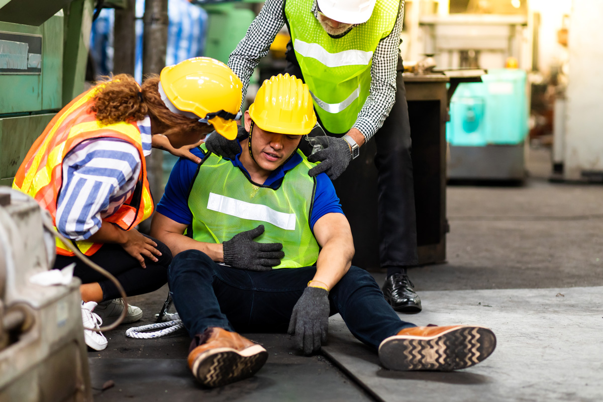 A worker in a yellow hard hat sitting on the floor with two people consoling him in El Paso.