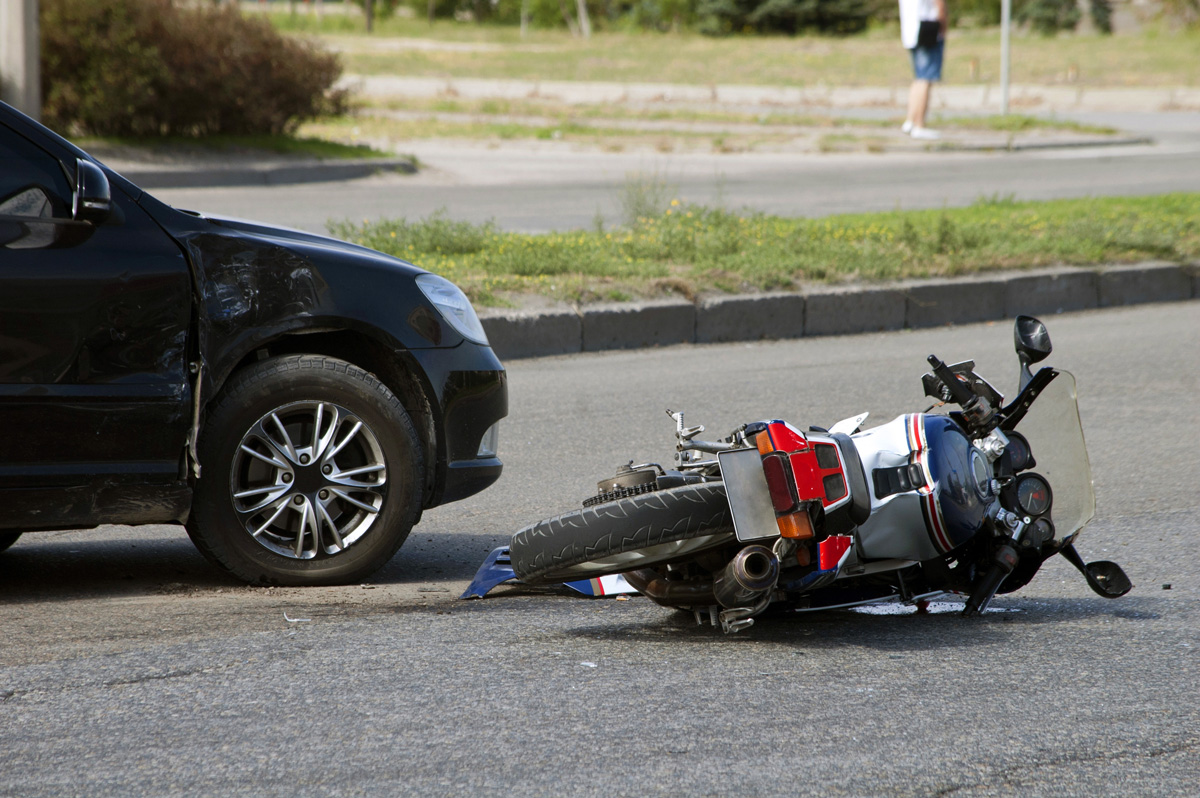 A motorcycle on its side in the road next to a black vehicle in El Paso.