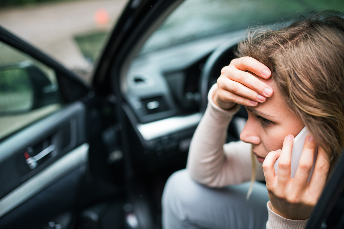 A woman sitting in her car with her hand on her forehead, talking on her cell phone in El Paso.