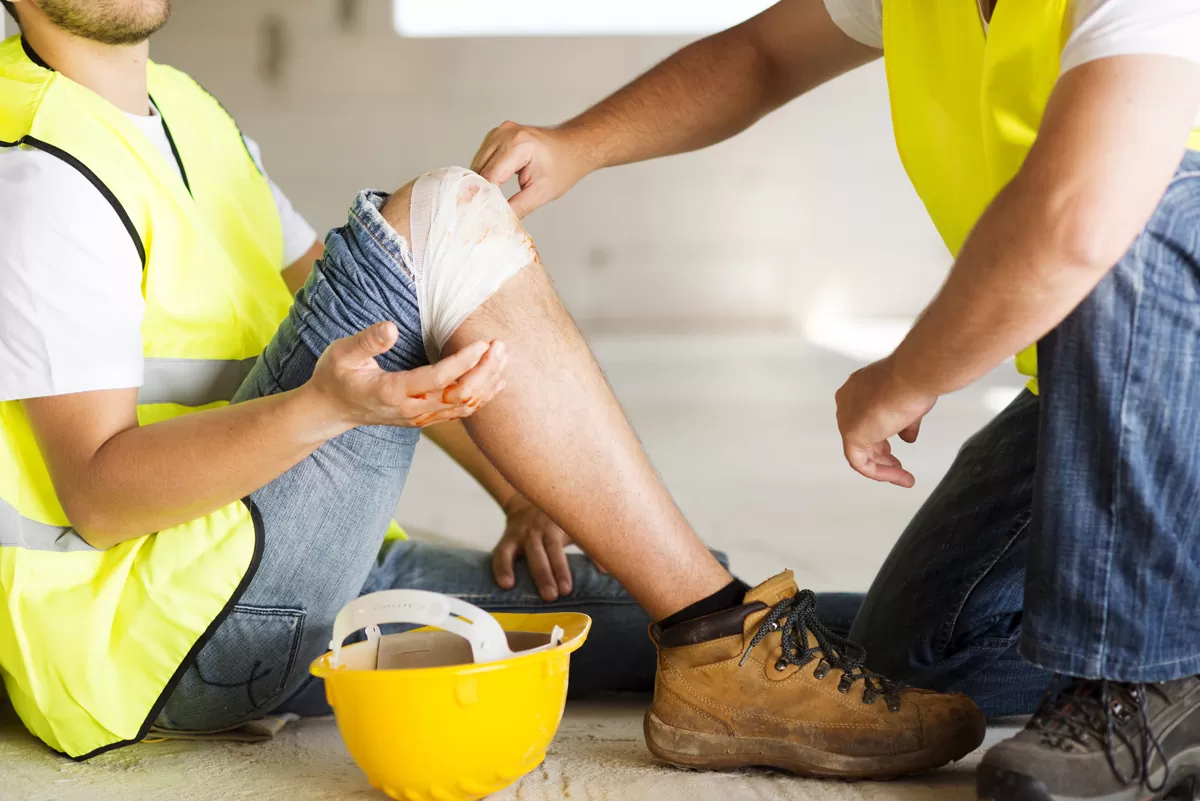 A worker in a bright yellow vest with a bandage around their knee and another worker assisting them in Missouri City.